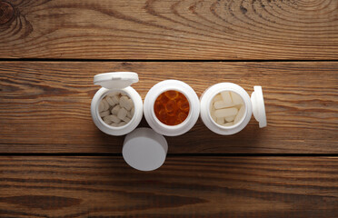 Different types of pills in white plastic bottles on a wooden table. top view