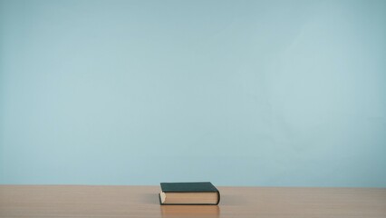 A book on a wooden table on a soothing pastel blue background.