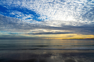Ciel bleu parsemé de nuages blancs au coucher de soleil, illuminant le sable mouillé d'une plage...