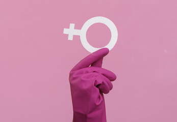 Feminism. Women's power. Hand in rubber cleaning glove holds a female gender symbol venev on a pink...