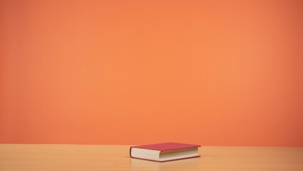 A red book on a wooden table on a bright orange background.