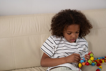 Focused African American young girl with curly hair, engaging with colorful beads, exemplifying...