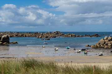 À marée basse, de petites embarcations reposent sur le sable, entourées d'amas rocheux, créant une scène pittoresque sur une plage bretonne.