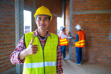 Young construction worker thumbs up happy smiling on a construction site. Confident architect engineering concept with worker in background copy space.