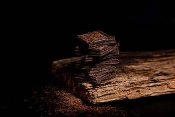 pieces of dark chocolate lie on top of each other, on a wooden plate