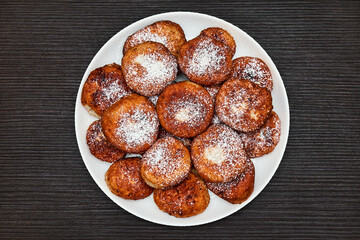 A round dish with fried pancakes on a brown table. Sweet dessert. Top view.