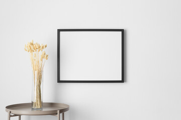Black frame mockup on the wall with a dry flower decoration.