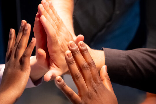 The image portrays a group of hands coming together in a high-five, symbolizing team success, unity, and collaboration. The diversity within the team is evident through the variety of skin tones