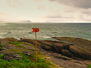 Warning sign on the rocks at the end of Boraceia beach during a summer storm - Translation of non-english text in the image - DANGER.