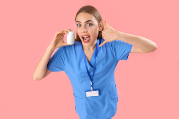 Female doctor with pill bottle showing "call me" gesture on pink background