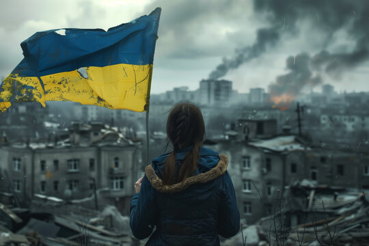 A woman holding Ukraine flag in a city with smoke in the background. The flag is torn and dirty