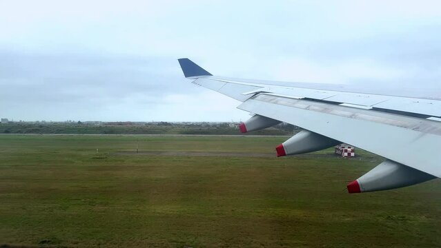 Airplane wing over green fields during landing approach, cloudy skies