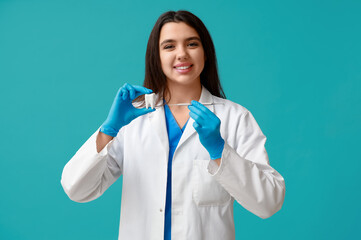Female dentist with tool and plastic tooth on blue background. World Dentist Day - obrazy, fototapety, plakaty