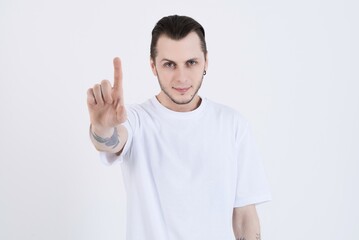 Attractive caucasian young man with tattoos in casual clothes looking at camera, giving advice and showing finger or number one isolated on white studio background