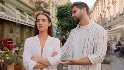 Young couple city annoyed offended angry woman arms crossed guilty man apologize quarrel outside...
