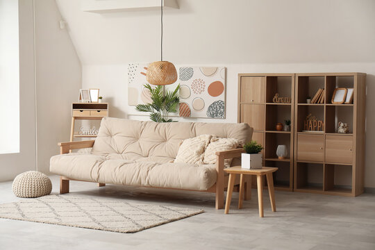 Interior of light living room with comfortable sofa, shelves and table