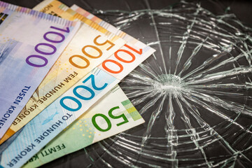 Norwegian money on broken glass, concept of weakness of Norwegian krone