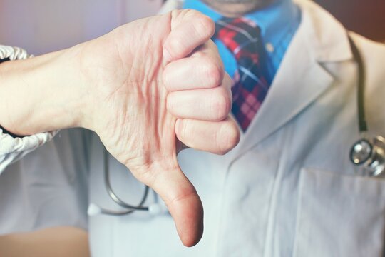 Man doctor in white coat with stethoscope show thumb down sign on gray background. Bad review, service, problems with treatment, medical care, ad and offer