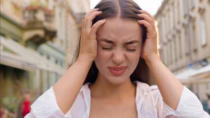 Close up young European Caucasian woman holding head headache migraine pain city outside unhappy...