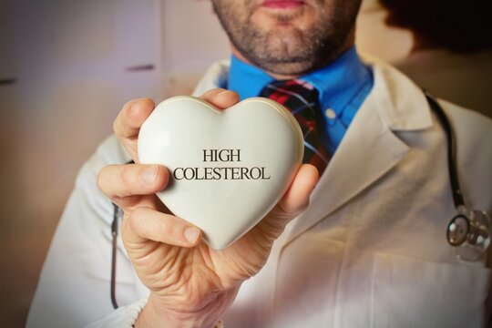 World Hypertension Day. Bearded doctor holds a white heart with text "High Colesterol", a symbol of high blood pressure. - Powered by Adobe