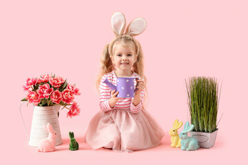 Cute little girl in bunny ears with tulip flowers, grass and toy rabbits on pink background. Easter celebration