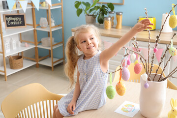 Cute little girl decorating willow branches with Easter eggs at home