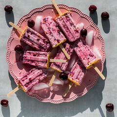 A platter of homemade cherry yogurt popsicles melting in bright sunlight.