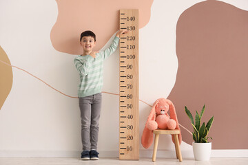 Surprised little boy pointing at wooden stadiometer near color wall