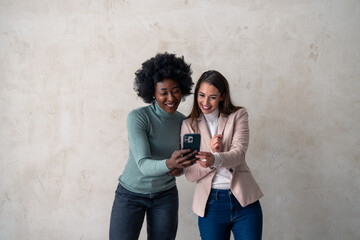 Cheerful young women with different skin tones looking at mobile phone screen while standing...