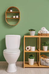 Interior of stylish bathroom with ceramic toilet bowl and houseplants on wooden shelving unit