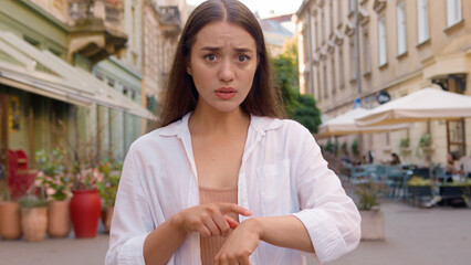 Caucasian european woman upset late time arms crossed showing hand watch angry displeased girl city...