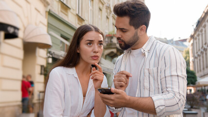 Couple Caucasian man woman using mobile phone smartphone internet maps location tourism trip tour GPS navigation app city center outside street confused male female attractions journey direction urban