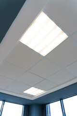 Fototapeta premium Square lamp on a white office ceiling. Interior design in the office. A fluorescent lamp on a modern suspended ceiling.