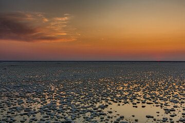 Obraz premium Sunset or sunrise on salt lake Elton (Russia) with mirror or reflection of low Cumulostratus or Stratocumulus clouds in the brine at golden hour with the sun in the background. Evening or morning.