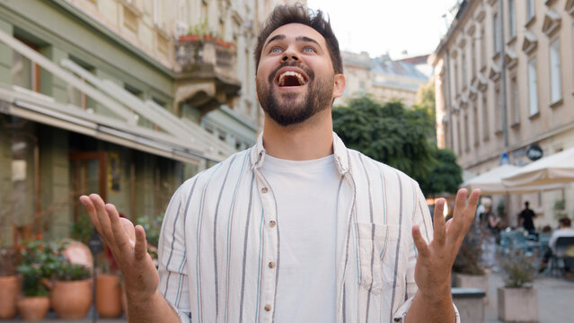Young Caucasian European man rejoice gesturing smiling victory success good luck shouting yes hurray city street outdoors enjoying delight happy guy amazed excited emotional male joyful astonishment
