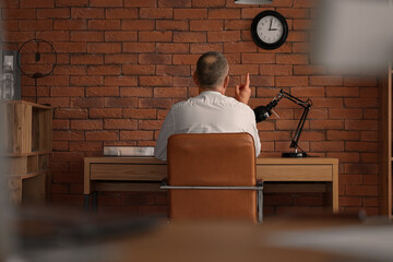 Mature businessman pointing at wall clock in office, back view
