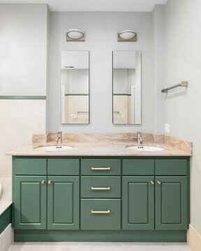 A bathroom with a green vanity cabinet, gold hardware, two mirrors, and a granite countertop.