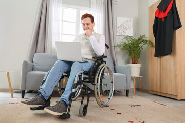 Male graduate in wheelchair using laptop at home