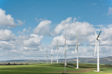 Wind turbines standing in rolling green hills under a cloudy sky for sustainable energy production - 753264854