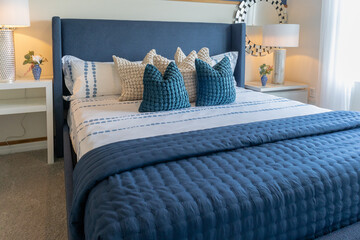 Front view of king size luxury bed with blue upholstered headboard in brightly lit master bedroom,...