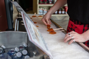 A traditional Canadian sweet candy made of boiled maple sap laid on a tray of clean snow. A male rolls thick syrup into round lollipops using a small wooden stick. A street vendor sells the pops.