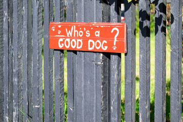 A vibrant red painted wooden sign with a funny saying: who's a good dog painted in white paint. The...