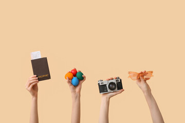 Female hands holding sunglasses with camera, passport and Easter eggs on beige background. Holiday...