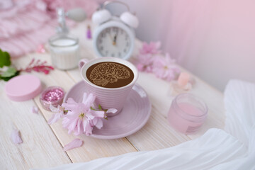 Obraz na płótnie Canvas Coffee cup, donut, sakura flowers, aromatic candles, romantic little things on white wooden table, concept of Relaxation Haven in boudoir, female life