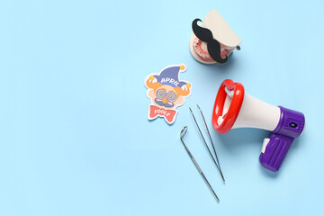 Model of jaw with paper mustache, megaphone and dentist tools on blue background. April Fools Day