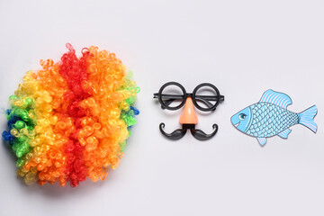 Clown wig with funny glasses and paper fish on white background. April Fools Day