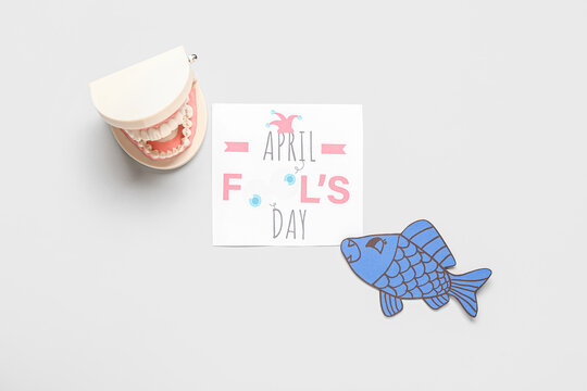 Sheet with text APRIL FOOL'S DAY, model of jaw and paper fish on white background