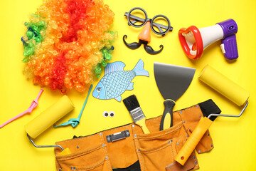 Belt with construction tools, paper fish and party decor on yellow background. April Fools Day