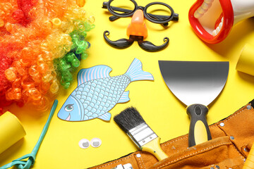 Belt with construction tools, paper fish and party decor on yellow background. April Fools Day