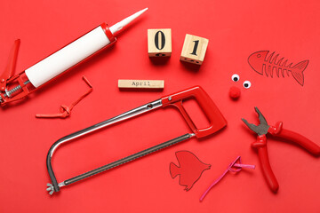 Calendar with mechanic tools, paper fishes and decor on red background. April Fools Day